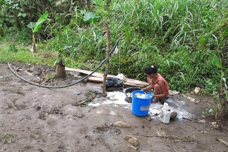 Eine Bewohnerin wäscht an einer Wasserstelle im Wald die Kleider ihrer Familie.