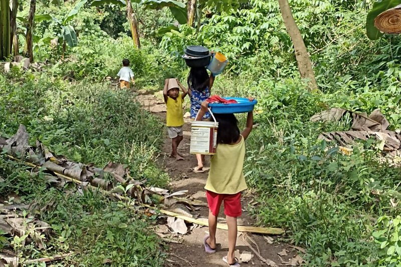 Kinder tragen gewaschene Kleider und Wasserbehälter von der Wasserstelle.